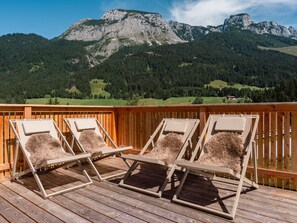 Une terrasse en bois, dotée de chaises longues et offrant une vue sur un paysage montagneux.