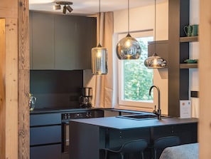 Une cuisine moderne dotée d’un îlot central, de luminaires suspendus et offrant une vue sur la verdure environnante.