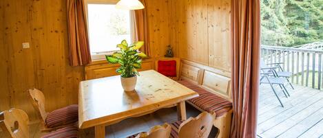 A wooden cabin with a dining table, chairs, a bench, and a view of a deck.