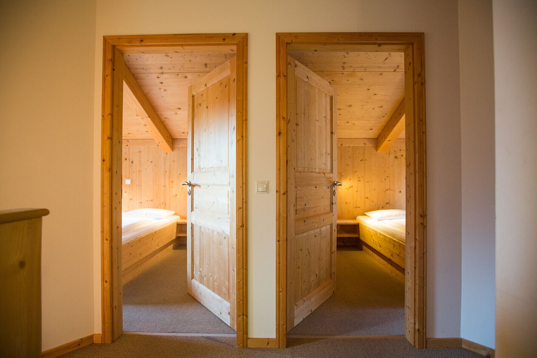 A narrow hallway with two wooden doors leading to bedrooms. Each room has a single bed and a nightstand.