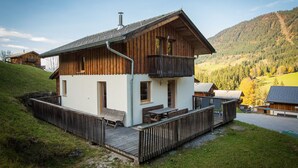 A wooden chalet with a balcony, a deck, and a view of a mountainous landscape.