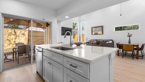 A modern kitchen with a large island, sliding glass doors to a patio, and a dining area with a table and chairs. - The Hidden Gem of Old City - Team Joseph Ellen (St Augustine)