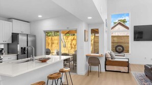 A modern kitchen with a central island, a dining area with a table and chairs, and a living space with a sofa and a TV mounted on the wall. - The Hidden Gem of Old City - Team Joseph Ellen (St Augustine)
