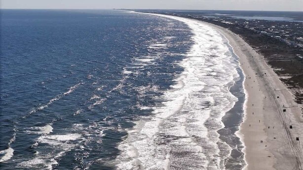 A coastal beach with a long stretch of sand, waves, and a few people. - The Hidden Gem of Old City - Team Joseph Ellen (St Augustine)