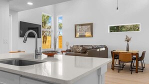 A modern kitchen with a large island, a dining area with a table and chairs, a sofa, and artwork on the walls. - The Hidden Gem of Old City - Team Joseph Ellen (St Augustine)