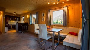 A cozy cabin interior with a dining area, kitchen, and a large window offering a mountain view.