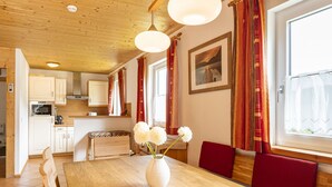 A wooden dining table with a white vase of flowers, red upholstered benches, and a kitchen in the background. - Chalet # 04 with 3 BR for 6 to 8 people (Annaberg)