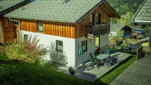 A two-story wooden house with a balcony, a deck with outdoor furniture, and a view of the surrounding landscape. - Chalet # 04 with 3 BR for 6 to 8 people (Annaberg)