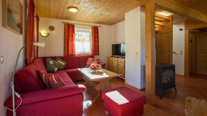 A cozy living room with a red sofa, a small table with fruit, a television, and a wood-burning stove. - Chalet # 04 with 3 BR for 6 to 8 people (Annaberg)