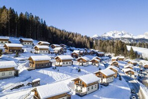 A snow-covered village with wooden cabins, a ski slope, and a mountain backdrop.