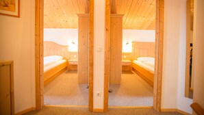 A room with two beds, wooden flooring, and a mirrored closet door.
