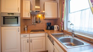 A kitchen with white cabinets, stainless steel appliances, a window with curtains, and a sink.