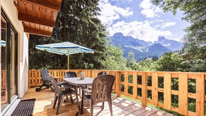 A wooden deck with a table and chairs, a striped umbrella, and a view of mountains.