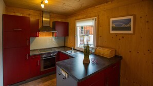 A compact kitchen with red cabinets, a stainless steel range hood, a sink, and a window with a view of a building outside. - Chalet # 92 with 3 BR for up to 6 people (Annaberg)