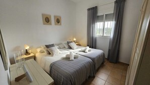 Une chambre d’hôtel avec deux lits, un bureau, une lampe et une fenêtre avec des rideaux.