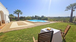 Un jardin avec une piscine, une table et des chaises sur une terrasse couverte.