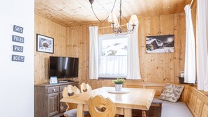Un intérieur en bois comprenant une table à manger, des chaises, un banc, un téléviseur et une fenêtre avec des rideaux.