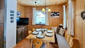 L’intérieur d’un chalet en bois chaleureux et accueillant, avec une table à manger dressée pour quatre personnes, un téléviseur et un banc agrémenté de coussins.
