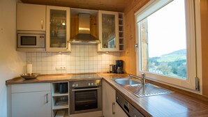 Una cocina moderna con horno empotrado, microondas y campana extractora de acero inoxidable. Hay una ventana que ofrece vistas al campo.
