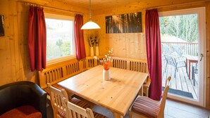 Un interior de madera con una gran mesa de comedor, cortinas rojas y vistas al exterior.