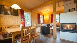Interior acogedor de una cabaña con una mesa de comedor de madera, sillas, un sofá y una chimenea.