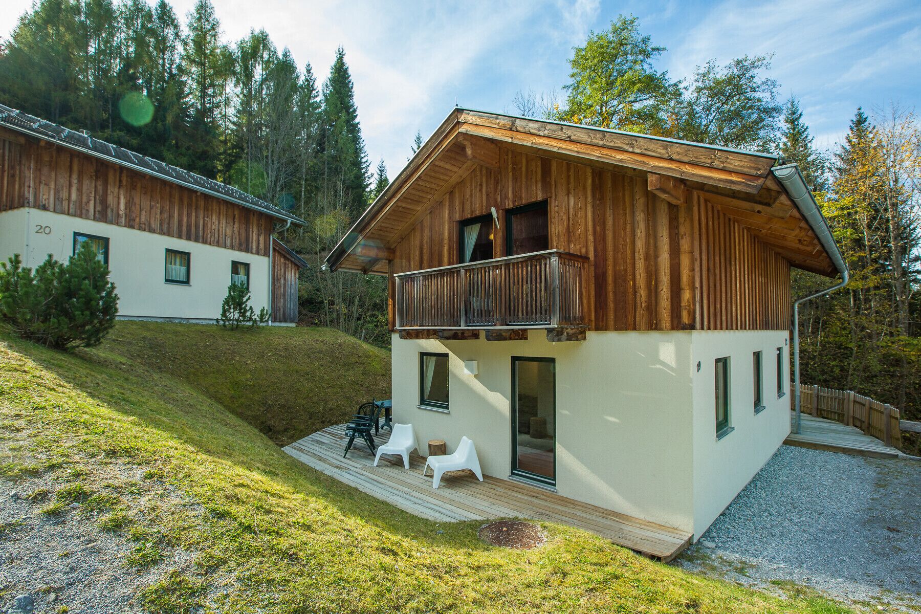 Un chalet moderne avec une façade en bois, un balcon et une terrasse dotée d’un espace salon extérieur.