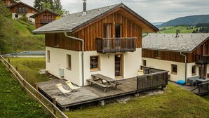Een chaletachtige constructie met een houten gevel, een balkon en een terras met lounge stoelen.