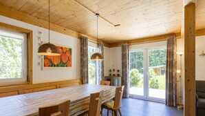 A dining area with a long table, wooden chairs, pendant lights, and a view through glass doors to the outside. - Chalet # 95 with 3 BR for up to 8 people (Annaberg)