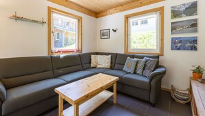 A modern living room with a sectional sofa, a wooden coffee table, and large windows with curtains. - Chalet # 95 with 3 BR for up to 8 people (Annaberg)