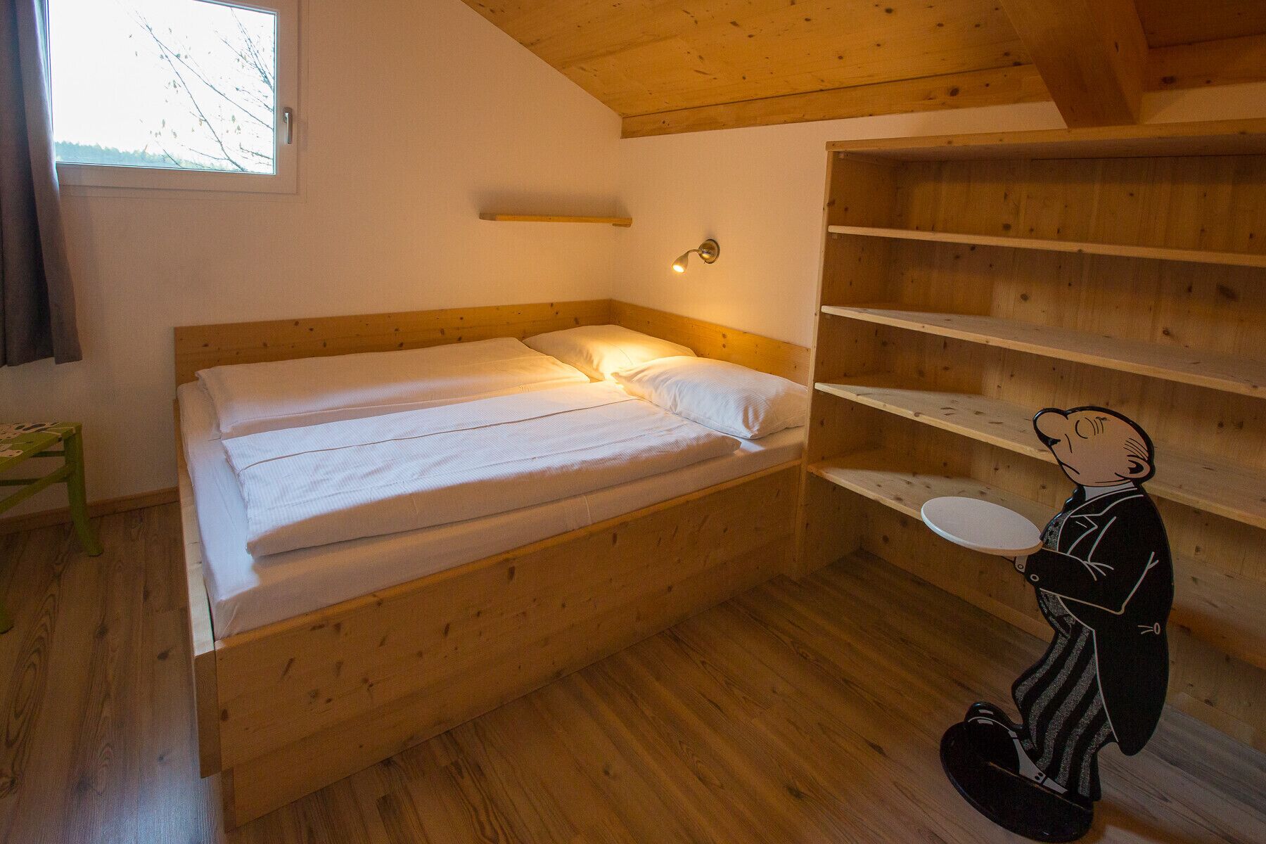 Una habitación pequeña y acogedora con una cama litera de madera, una mesita y una estantería.