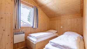 A small, wooden cabin bedroom with two beds, a window with curtains, and a wall-mounted heater. - Chalet  # 72 with 4 BR and infrared sauna (Annaberg)