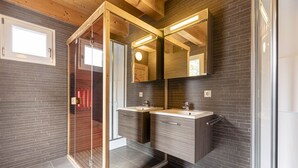 A modern bathroom with a glass shower enclosure, two sinks, and a large mirror. - Chalet  # 72 with 4 BR and infrared sauna (Annaberg)