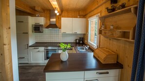 A compact kitchen with wooden cabinets, a stainless steel oven, a microwave, a sink, and a window providing natural light. - Chalet  # 72 with 4 BR and infrared sauna (Annaberg)