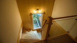 En trætrap med et vindue foroven, der fører op til en balkon med udsigt over grønne omgivelser.