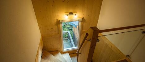 A wooden staircase with a window at the top, leading to a balcony with a view of greenery.
