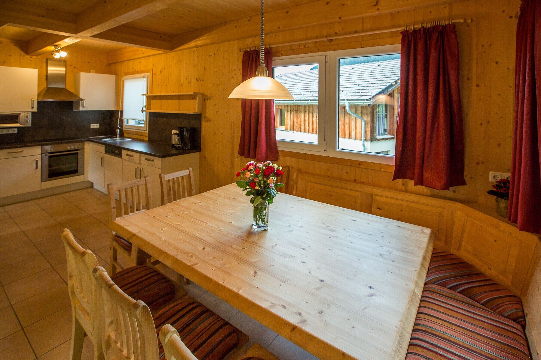 Un intérieur en bois comprenant une table à manger, des chaises, un vase de fleurs et un coin cuisine.