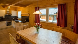 Un intérieur en bois comprenant une table à manger, des chaises, un vase de fleurs et un coin cuisine.