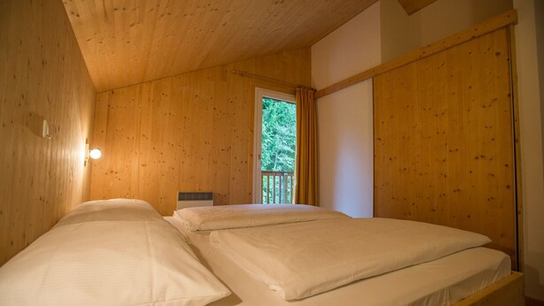 Une chambre avec deux lits, des murs en bois, une fenêtre avec des rideaux et un balcon visible.