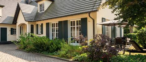 A traditional European-style building with a tiled roof, green shutters, and a paved courtyard.