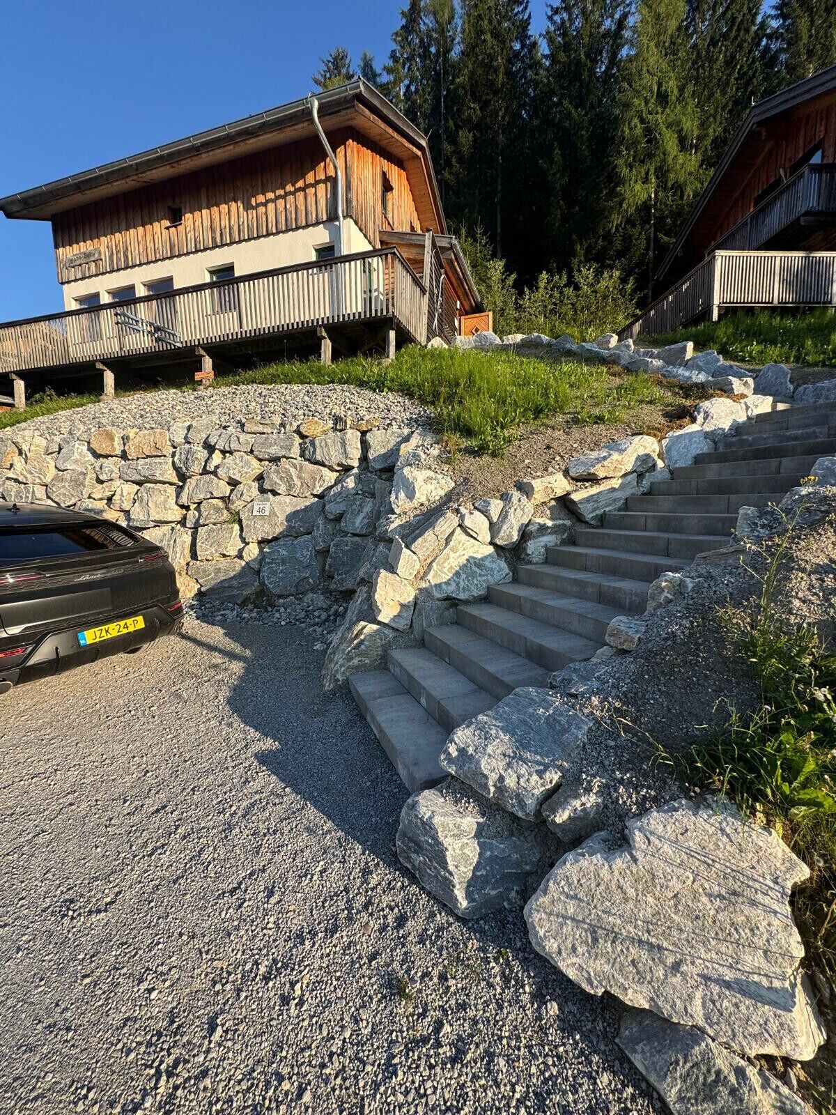 Rakennuksessa on kivestä rakennettu portaikko, joka johtaa puiseen terassiin, ja sen ympärillä on puita.