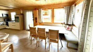 Un interior de madera con una mesa de comedor, sillas, un banco, una zona de cocina y una ventana con cortinas.