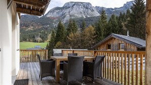 Una terraza de madera con una mesa y sillas, con vistas a un paisaje montañoso.