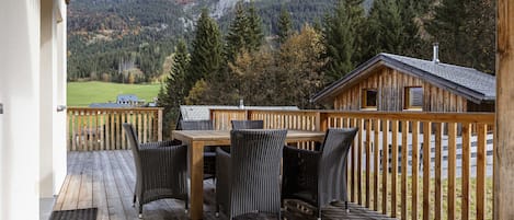 A wooden deck with a table and chairs, overlooking a mountainous landscape.
