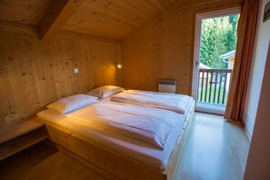 A wooden cabin bedroom with two beds, a small heater, and a balcony with a view of trees. - Chalet  # 82 with 4 BR for up to 8 people (Annaberg)