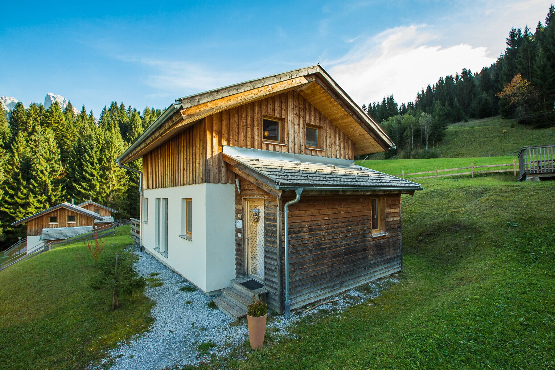 Un chalet en bois avec un toit en pente, une partie blanche sur le côté gauche et une allée gravillonnée.