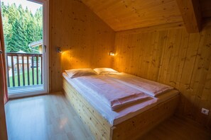 Une petite chambre aménagée dans une cabane en bois, avec un lit simple, une fenêtre donnant sur une forêt et un balcon.