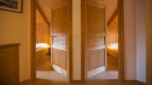 Un intérieur en bois avec deux portes ouvertes donnant sur une chambre à coucher équipée d’un lit et d’une table de chevet.