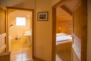 Une cabane en bois avec une salle de bain et une chambre. La salle de bain est équipée de toilettes, d’un lavabo et d’une douche. La chambre comprend un lit et une fenêtre.