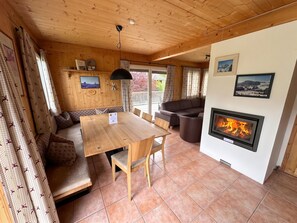 L’intérieur d’un chalet accueillant, avec une table à manger en bois, un canapé, une cheminée et une vue sur l’extérieur.