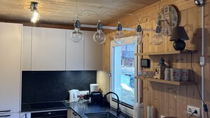 Une cuisine moderne avec des meubles en bois, un plan de travail noir et un four encastré. Des luminaires suspendus et une fenêtre laissent entrer la lumière naturelle.